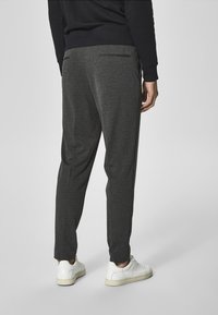 Szare spodnie dresowe o luźnym kroju, wyposażone w boczne kieszenie i ściągacze na nogawkach. Noszone z białymi trampkami, na neutralnym, gładkim tle.