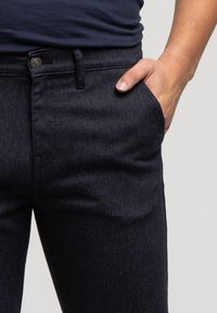 Ciemne dżinsy z delikatną teksturą. Posiadają przednią kieszeń i zapięcie na guzik. Klasyczny krój z nowoczesnym designem.