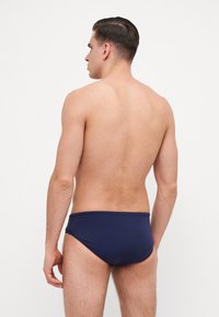 Calções de banho azul-marinho feitos de material elástico, apresentando uma textura suave e um design simples, sem padrões ou realces visíveis.