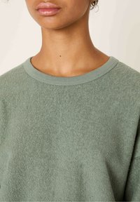 Sweatshirt verde, con texture, caratterizzato da un colletto a girocollo e bordo a coste. Il tessuto ha un aspetto morbido e peloso.