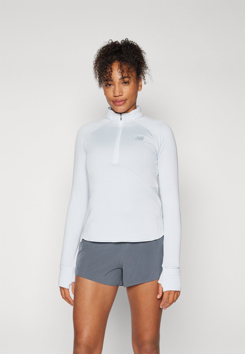 Helles blaues Longsleeve-Oberteil mit Viertelreißverschluss und strukturiertem Muster, ergänzt durch Daumenlöcher, kombiniert mit dunkelgrauen Shorts.