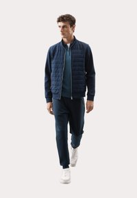 Marineblå quiltet jakke med sølv lynlås, blå pullover og matchende joggers, suppleret med hvide sneakers. Glat stofstruktur hele vejen igennem.