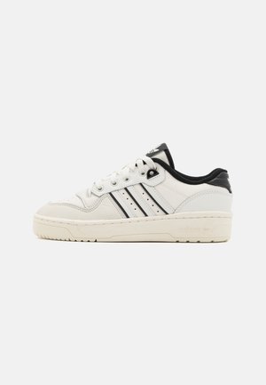 Fehér bőr sneaker fekete részletekkel, perforált mintázattal, háromsávos dizájnnal, kerek orral és texturált gumitalppal.