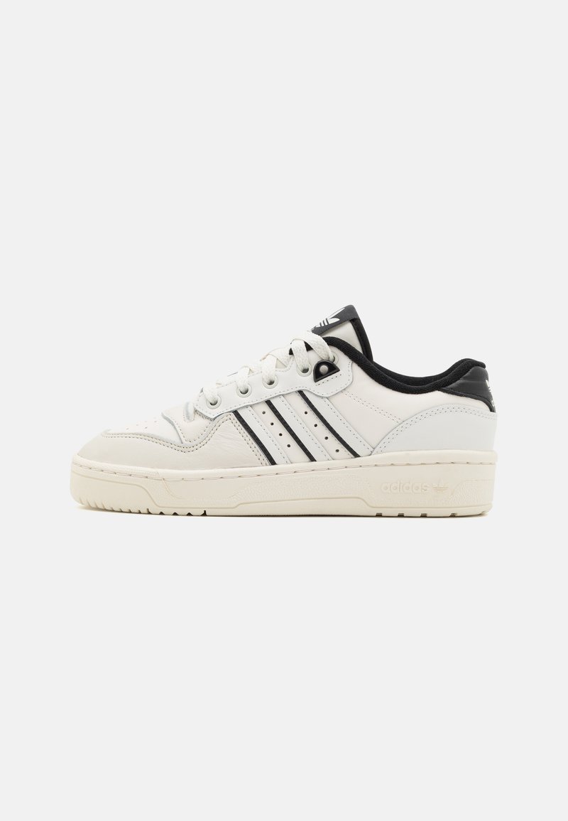 Fehér bőr sneaker fekete részletekkel, perforált mintázattal, háromsávos dizájnnal, kerek orral és texturált gumitalppal.