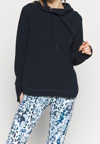 Granatowa bluza z kapturem ze sznurkiem, miękka tkanina i przednia kieszeń. Do tego niebiesko-białe legginsy z abstrakcyjnym wzorem.
