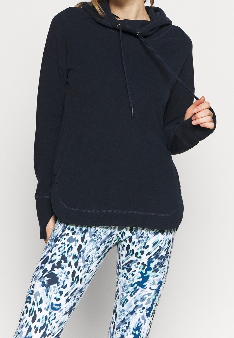 Granatowa bluza z kapturem ze sznurkiem, miękka tkanina i przednia kieszeń. Do tego niebiesko-białe legginsy z abstrakcyjnym wzorem.