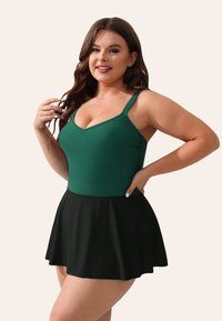 Groene zwemtop met een v-hals en dunne schouderbandjes, gecombineerd met een uitlopende zwarte rok. Soepele stof met een getailleerde taille en een vloeiende ondersectie.