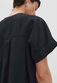 Top nero a maniche corte con scollo rotondo e tessuto morbido e testurizzato. Presenta una cucitura a yoke sulla schiena per un dettaglio in più.