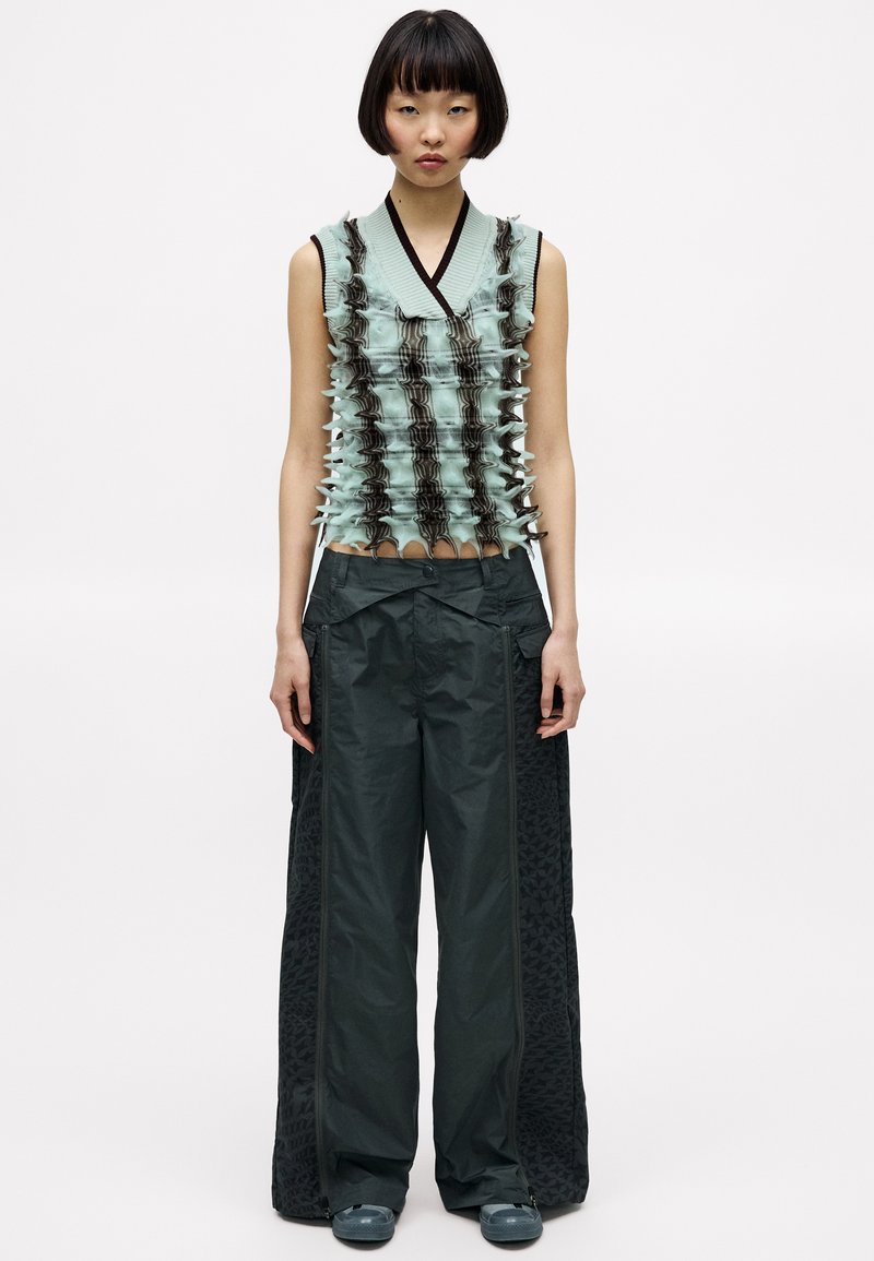 Ljusblå ärmlös topp med texturerad detalj och mörka accenter, kombinerad med löst sittande mörka byxor med ett mönstrat sidopanel.