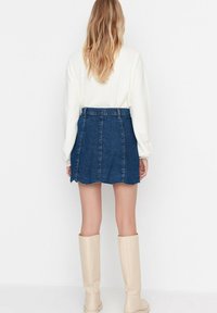 Denim mini-jurk met een rafelige zoom, met een hoge taille en verticale naden. Gepaard met kniehoge crèmekleurige laarzen.