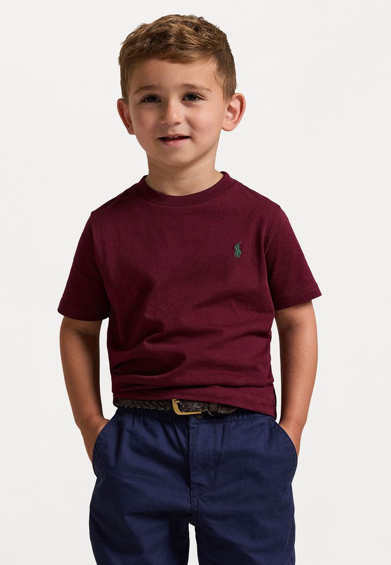 Κερασί μπλούζα βαμβακερή με στρογγυλή λαιμόκοψη και κοντά μανίκια, με ένα μικρό πράσινο λογότυπο, σε συνδυασμό με σορτς ναυτικού χρώματος με ελαστική μέση.