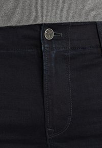 Donkerdenim jeans met een soepele textuur, voorzien van een metalen knoopsluiting, contrasterende stiksel en slim-fit ontwerp bij de tailleband.