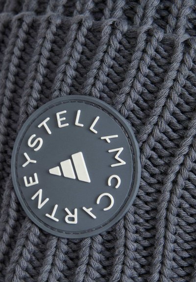Tissu tricoté gris foncé avec une étiquette ronde noire présentant un texte blanc et un logo triangulaire au centre.