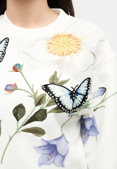 Λευκό φούτερ με κεντητά μεγάλα λευκά και μπλε λουλούδια, πράσινα φύλλα και λεπτομερές μπλε-μαύρο πεταλούδα στο στήθος.