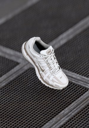 Nike jooksujalatsid off-white võrgust hallide aktsentidega, millel on pehme tallaga ja keeruline paeladisain. Nähtav tekstureeritud pinda profiil.