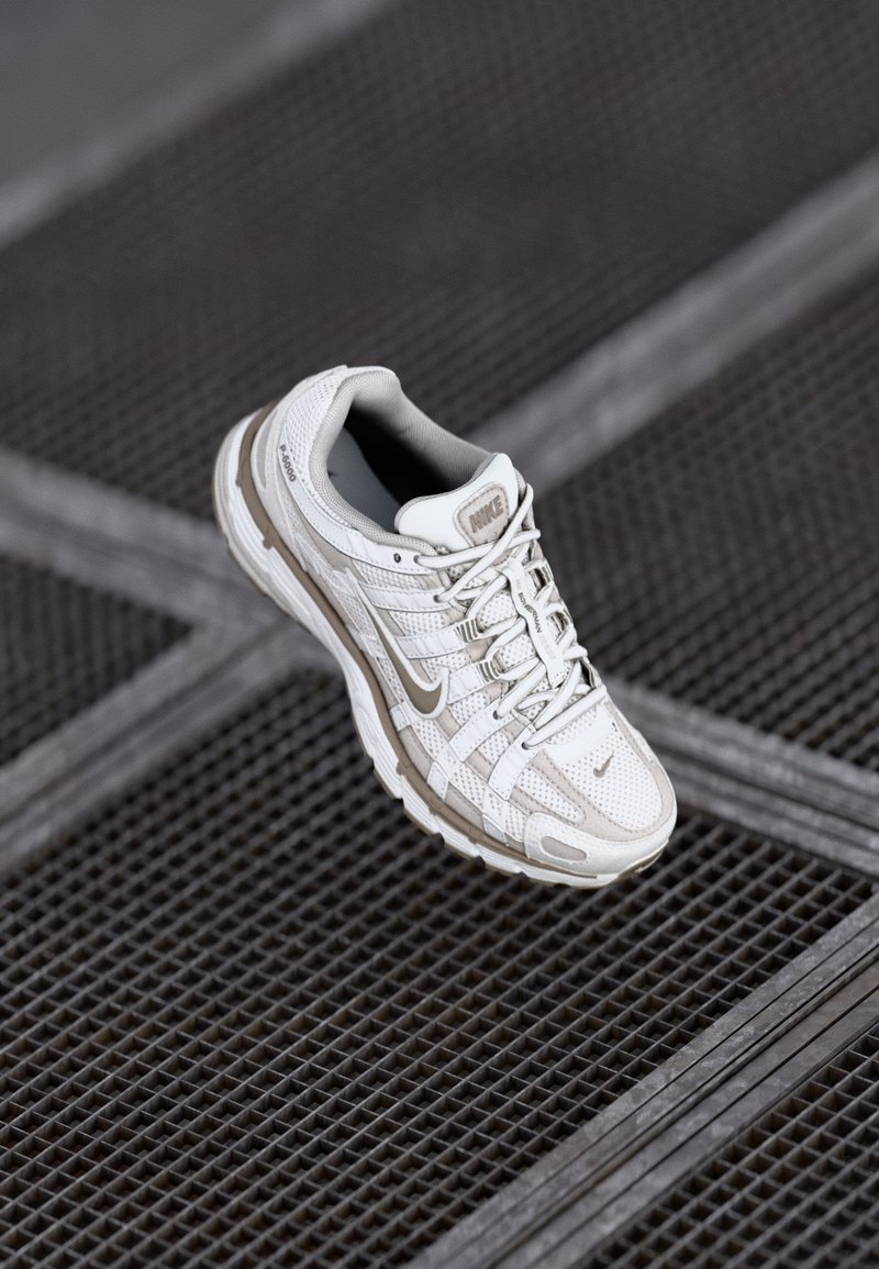 Nike-Laufschuh aus off-white Mesh mit grauen Akzenten, ausgestattet mit einer gepolsterten Sohle und einem filigranen Schnürdesign. Texturierte Oberflächenprofil sichtbar.