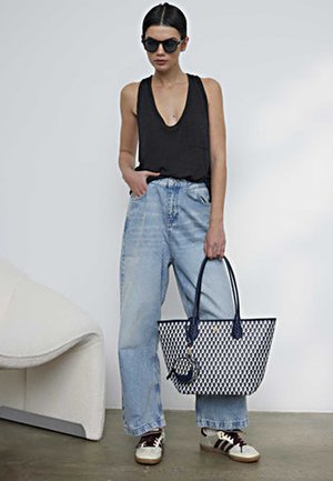 Débardeur noir sans manches, jean large bleu clair, baskets blanches avec des accents marron et un sac fourre-tout noir et blanc à motif avec des poignées bleues.