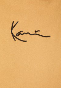 Tissu jaune moutarde présentant une signature noire brodée. La texture est lisse avec un motif de tricotage régulier.