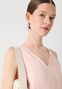 Lys rosa ermeløs topp med v-hals, glatt tekstur. Sølv kuleøredobber og en beige bagestropp gir kontrast. Rent, minimalistisk design.