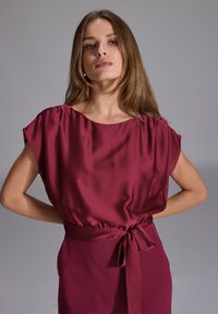 Bordowy satynowy top z krótkimi rękawami, luźny krój i związany w talii, tworzy gładkie linie i subtelną poświatę.