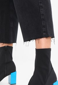 Svart denim med fransad nederkant kombinerat med en svart ankelboots med en kontrasterande blå blockklack och sidoglidå.