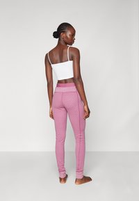 Rózsaszín, mintás leggings, bordázott derékkal, egy fehér, testhezálló toppal párosítva. A leggings kiterített szárakkal és sima textúrával rendelkezik.