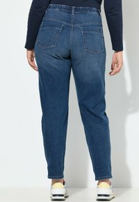 Vaqueros de mezclilla azul con pierna ajustada, cinturilla elástica y dos bolsillos traseros. Textura suave con un acabado de lavado medio.