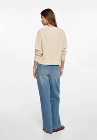 Beige stickad tröja med oversized passform, ribbade muddar och fåll, tillsammans med ljusblå vida jeans som visar bakfickor och en viss blekning.