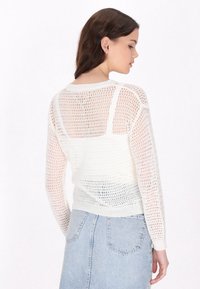 Witte gebreide trui met een losse, open gaasdesign, lange mouwen en ribgebreide mouwen. Heeft een ronde hals en een relaxte fit.