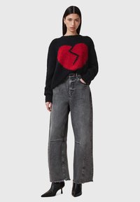 Schwarzer, flauschiger Pullover mit einem auffälligen roten Herzmotiv, kombiniert mit hoch taillierten grauen weit geschnittenen Jeans. Schwarze Knöchel-Stiefel runden das Outfit ab.