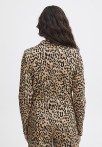 Blazer con stampa leopardata in beige e nero. Texture liscia, vestibilità sartoriale con una leggera lucentezza, con colletto a punta e maniche lunghe.