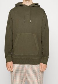 Olivgrön huvtröja med framficka, justerbara snören, ribbade ärmslut och nederkant. Diskret logotypdetalj på bröstet.