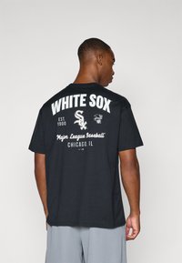 Crna majica s kratkim rukavima na kojoj je s leđa u velikim bijelim slovima ispisano "WHITE SOX", uz logotipe tima i dopunski tekst.