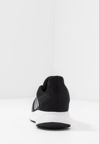 Czarne buty sportowe z przewiewną siateczkową cholewką, białą podeszwą środkową i charakterystycznym paskiem po stronie. Gładka, elastyczna podeszwa z gumy.