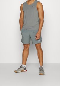 Graues ärmelloses Sportshirt und graue Shorts mit schwarzen Nike-Logos. Graue und weiße Sneakers mit roten Akzenten und Gummisohlen. Weiße Socken.