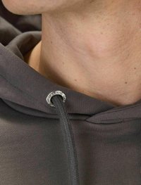 Grå huvtröja med en slät textur, med en metallöga för snöret. Närbild som visar halsringningen och detaljerna på snöret.