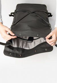 Schwarzer wasserdichter Rucksack mit einem Reißverschlussfach und einem geometrisch gemusterten Innenraum, ausgestattet mit verstellbaren Trägern und Druckknopfverschlüssen.