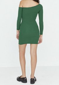 Grön ribbad klänning med avskuret axelparti och långa ärmar, figursydd design, längd ovanför knäna, i kombination med svarta platåsandaler.