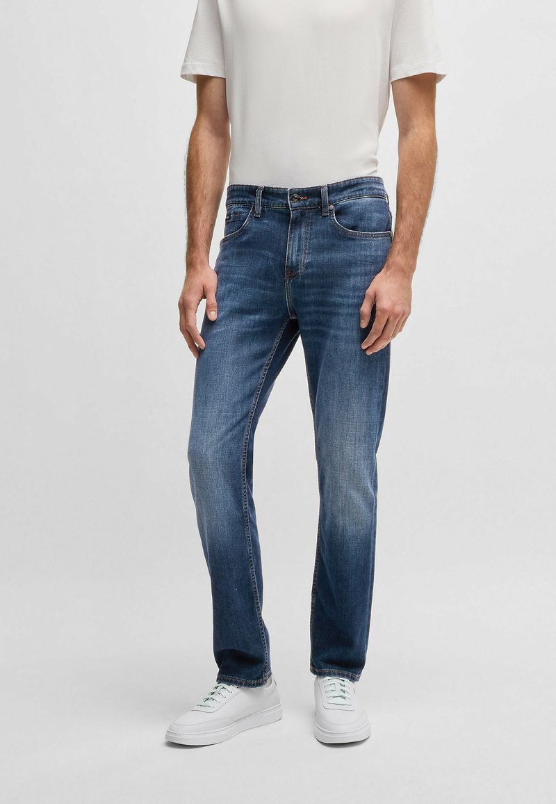 Blå denimjeans har en rak passform, urblekta partier, klassisk femfickdesign, och är kombinerade med en enkel vit t-shirt och vita sneakers.