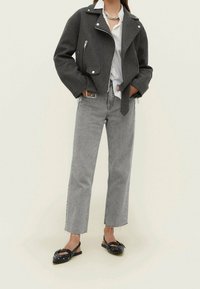 Veste grise courte avec fermeture éclair sur le devant, garnitures argentées et manches larges, associée à un jean gris taille haute et des ballerines noires cloutées.