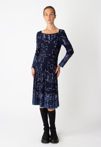 Robe bleu marine à manches longues, décolleté carré, motif floral, jupe plissée et taille cintrée, associée à des chaussettes noires montantes.