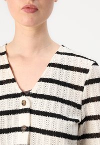 Pletený cardigan s V-krkem, béžový s černými pruhy, ozdobnými knoflíky, otevřenou pleteninou a krátkými rukávy.