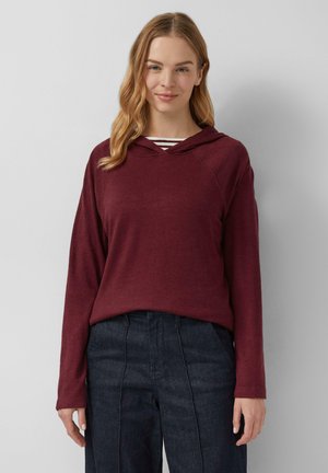 Bordeaux hoodie met lange mouwen en een V-hals ontwerp, laag over een gestreept topje, gecombineerd met donkere wijde broek.