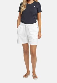 Granatowy t-shirt z małym logo, zestawiony z białymi bawełnianymi szortami z elastycznym pasem i bocznymi kieszeniami. Płaskie sandały.