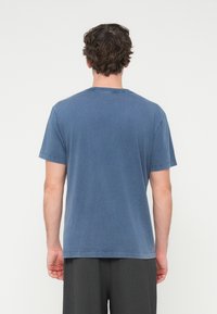 Μπλε βαμβακερό μπλουζάκι με κοντά μανίκια, στρογγυλή λαιμόκοψη και άνετη εφαρμογή. Λείο υλικό με μίνιμαλ σχεδιασμό. Εμφανίζεται η πίσω όψη.