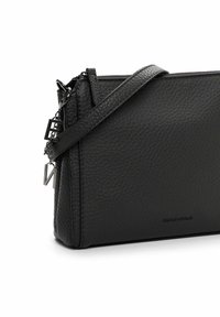 Borsa a tracolla nera in pelle texture con chiusura a zip, tracolla sottile e charm in metallo a forma di lettere appesi sul lato.