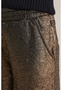 Metālisku bronzas sporta bikses ar teksturētu virsmu un sānu kabatām. Iekļautas ribotas jostas vietas un neliela logo birka blakus kabatai.