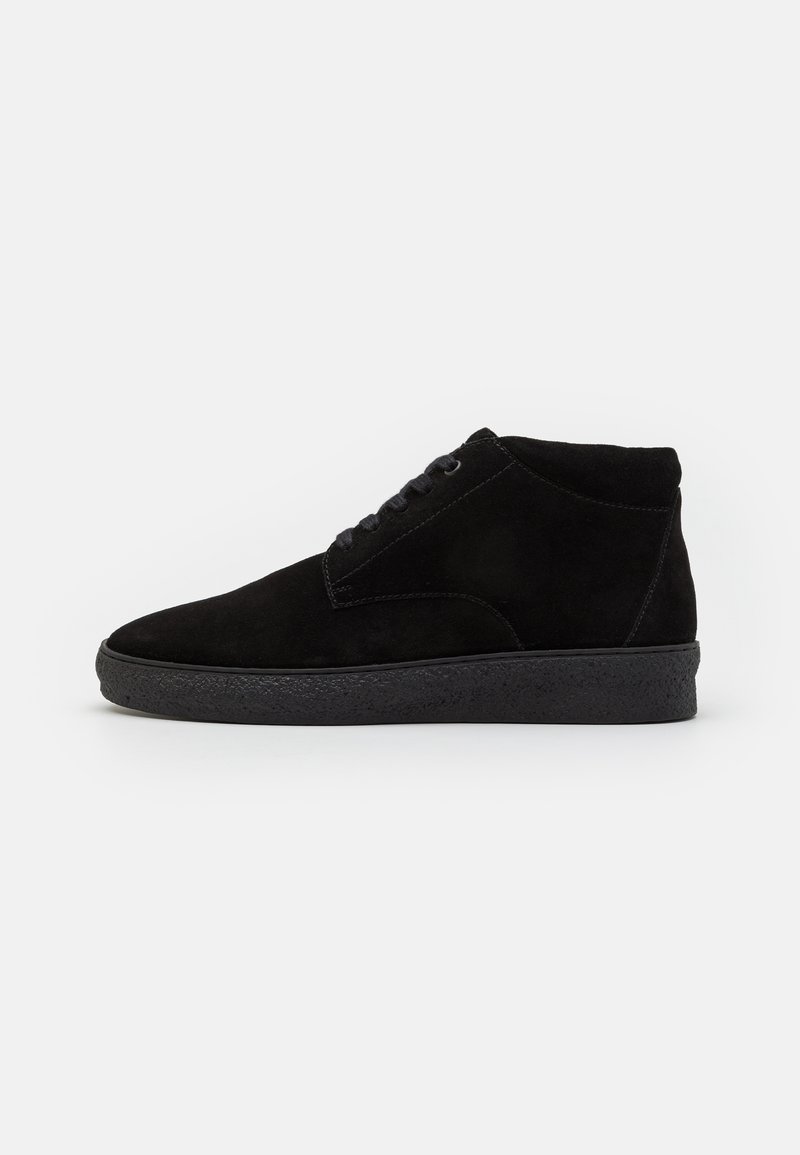 Sapatos high-top de camurça preta com bico redondo, frente com atacadores e sola texturizada de borracha preta. Superfície lisa com detalhes de costura mínimos.