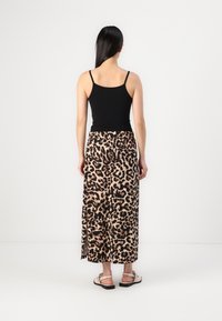 Jupe longue à imprimé léopard avec une taille noire, fabriquée en tissu léger. Portée avec un débardeur noir et des sandales claires.