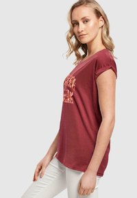Bordeaux t-shirt med rullede korte ærmer, der har et tekstureret grafisk design i lysere farver på forsiden. Blød, afslappet pasform.